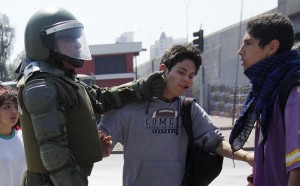 A riot police officer punches a student during a protest against the government and the public state education system at Santiago city